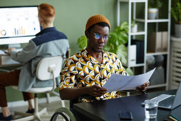 Portrait of black young man reading documents and wearing creative style while working in office