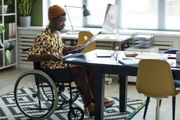 Full length portrait of black young man in wheelchair wearing creative fashion while working in...