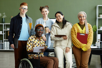 Portrait of diverse creative team looking at camera with cheerful smiles while posing in office, wheelchair user inclusion