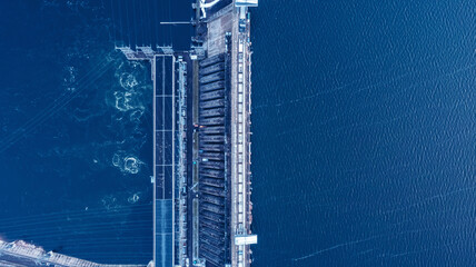 Aerial top view hydroelectric dam, water discharge through locks, blue color banner industrial...