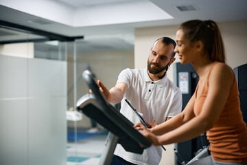 Fitness instructor assists sportswoman in using stationary bike at health club.