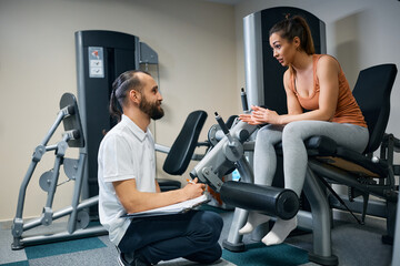 Fototapeta premium Athletic woman and her fitness instructor talk while making exercise plans in a gym.