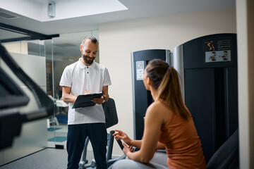 Happy personal trainer makes training plans with athletic woman in health club.