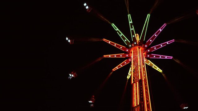 4K very high merry-go-round spinning in night sky at amusement park. Amusement park environment concept.
