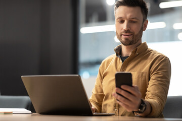 Fototapeta na wymiar Businessman Using Mobile Phone Sitting Near Laptop In Modern Office