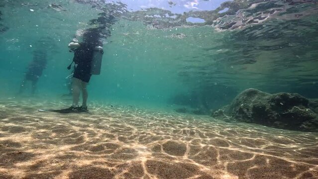 Under Water Film 4k - Thailand - 1 meter deep water - divers standing on the ocean floor - sprinkled  rays of sunlight covering the sand and rocks - tropical fish