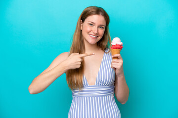Young caucasian woman in swimsuit eating ice cream isolated on blue background and pointing it
