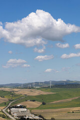 Fototapeta na wymiar Green landscape in Cadiz, Spain, with some windmills to supply power, and with cumulus clouds