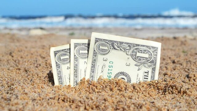 Paper bills one dollar buried in the sand on the beach against backdrop of sea close-up. American dollars cash banknotes of one dollar denomination in sand in sunny summer day. Money finance concept