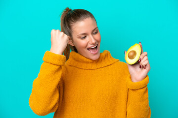 Young caucasian woman holding an avocado isolated on blue background celebrating a victory