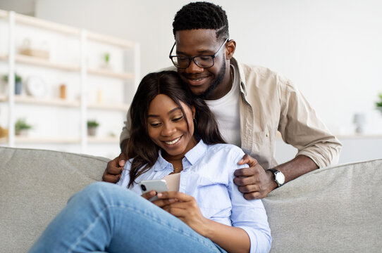 African american couple sitting on couch, using mobile phone