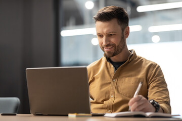 Cheerful Entrepreneur Using Laptop And Taking Notes Working At Workplace