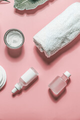Beauty setting background with various cosmetic products: bottles, moisturizing facial creme and towel on pink background. Healthy modern skin care. Top view.
