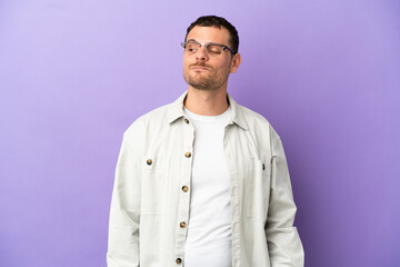 Obraz premium Brazilian man over isolated purple background having doubts while looking side