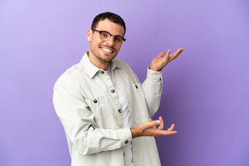 Brazilian man over isolated purple background extending hands to the side for inviting to come