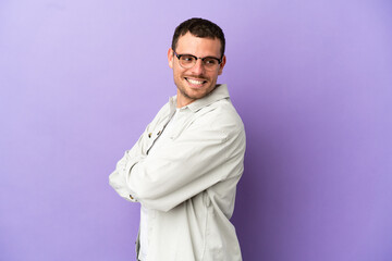 Brazilian man over isolated purple background with arms crossed and happy