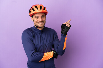 Young Brazilian cyclist man isolated on purple background pointing finger to the side - obrazy, fototapety, plakaty