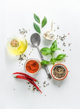 Healthy ingredients for food flavoring: olive oil, basil leaves, chili, garlic, pepper, bay leaves and spoon on white background. Cooking preparation with herbs and spices. Top view.