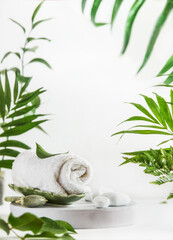 Obraz na płótnie Canvas Spa setting with towel, jade massage roller and stones on white podium at white background with tropical leaves. Modern skin care treatment . Beauty products. Front view.