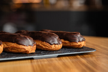 Tasty chocolate eclairs on slate plate in cafe. Delicious pastries for coffee. Isolated eclairs on the wood table