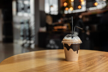Iced coffee or latte in take away plastic cup on cafe table. Disposable transparent plastic coffee cup isolated in coffee shop. Chocolate coffee cocktail