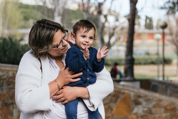 Happy mother holding her little son in arms while enjoying time together outdoors in a park.