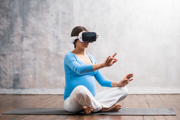 Young pregnant woman in VR helmet. She is preparing for the birth of a child on a virtual simulator at home. Augmented reality technology.