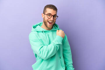 Young handsome caucasian man isolated on purple background celebrating a victory