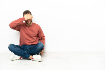 Young handsome man sitting on the floor covering eyes by hands. Do not want to see something