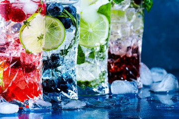 Fototapeta Cold summer cocktails drinks. Classic alcoholic long drink and mojito or mocktail in highballs with blueberries, blackberries, raspberries, lime, herbs and ice on blue background obraz