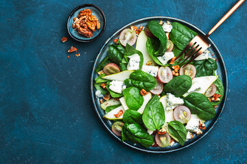 Delicious summer salad with pear, grapes, roquefort cheese, spinach, walnuts on blue table background, top view, negative space