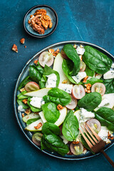 Delicious summer salad with pear, grapes, roquefort cheese, spinach, walnuts on blue table background, top view, negative space