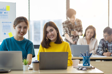 Fototapeta premium Portrait of a young woman working in the office with coworkers working in the background. Looking at camera.
