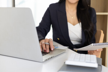 Attractive businesswoman working on laptop close-up writing work memo on notepad.