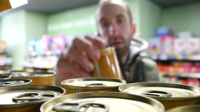 Close-up of many beautiful tin cans on a supermarket shelf and a man takes one