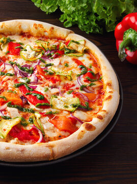 Vegan pizza with vegetables and pesto sauce on a wooden background. Gluten-free pizza with zucchini, red pepper, purple onion, cheese. Menu of cafes, pizzeria, restaurant. Close up. Copy space. Fresh