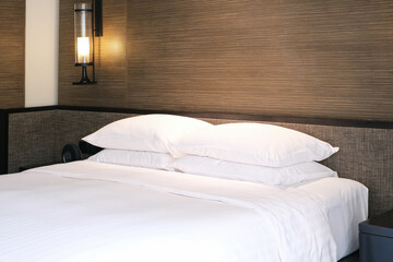 Clean Bedding sheets and pillow on natural wall room background. White bedding and pillow in hotel room. White pillows on empty bed.