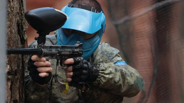 Portrait of american paintball player in mask who is aiming in opponents at war arena. Paintball player in a mask who is aiming at opponents. Man takes aim and shoots at enemy