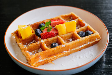 Waffle with Fresh Fruits. Waffles with berries and icing sugar on a white plate. Waffles with strawberries, blueberries, mango and sugar, homemade breakfast.