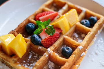 Waffle with Fresh Fruits. Waffles with berries and icing sugar on a white plate. Waffles with strawberries, blueberries, mango and sugar, homemade breakfast.