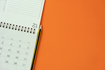 close up of calendar and pencil on the orange table background, planning for business meeting or travel planning concept