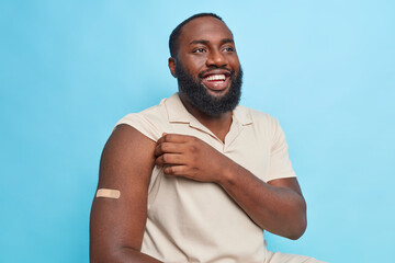 Bearded dark skinned adult man shows arm with plaster after coronavirus vaccination gets vaccine...