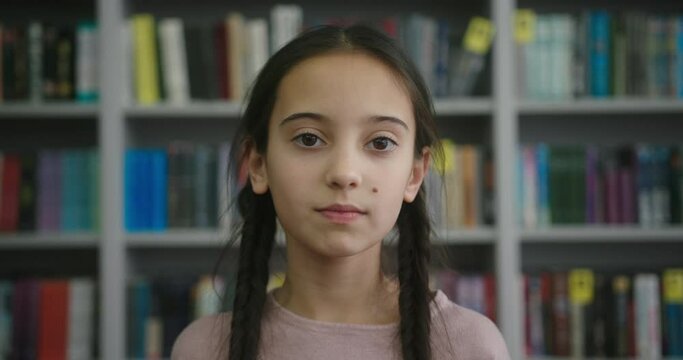 Asian girl with braids looks in camera smiling in library