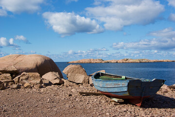 Landscape with ocean and an old worn fishing boat among red granite rock slabs at Stångehuvud...