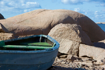 Landscape with ocean and an old worn fishing boat among red granite rock slabs at Stångehuvud...