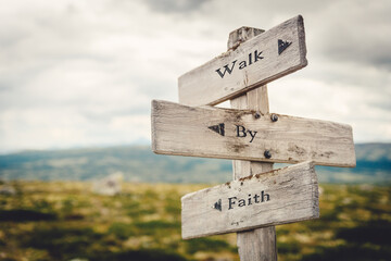 walk by faith text quote written in wooden signpost outdoors in nature. Moody theme feeling.