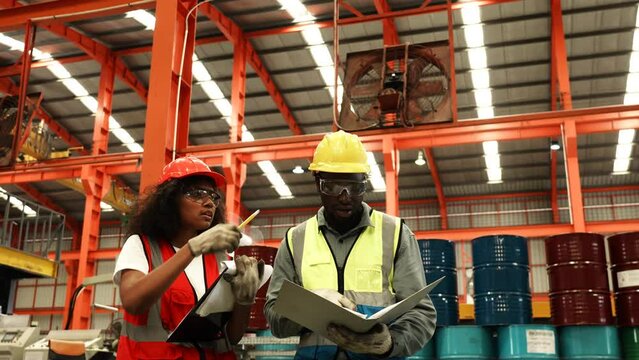 Two engineer worker together, Woman writing on clipboard. Man checking on document folder. Two people wear safety uniform and helmet to work check in factory, Warehouse workshop for factory industrial