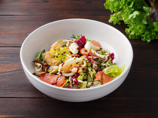 Recipe for fresh seafood salad in bowl on a wooden background. Shrimp, squid, green salad, sauce. The concept of healthy eating. Healthy food. Top view. Copy space. Close up. Mediterranean dish. Lunch