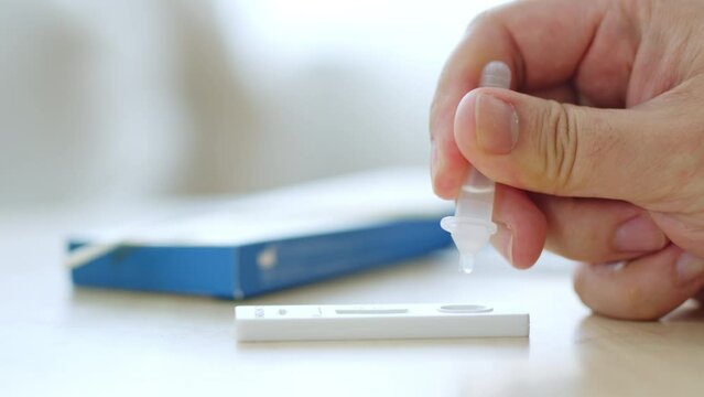 CLoseup hand using rapid antigen test kit (ATK) for self test at home. Dropping sample fluid on test kit. Pandemic of disease, covid-19, coronavirus