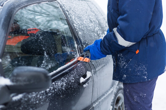 A human hand in a glove cleans a blue car from snow with a special brush. A hand sweeps snow from the hood of the car. Horizontal photo. the consequences of a blizzard